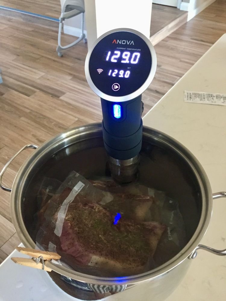 Vacuum-sealed seasoned meat in a stainless pot with a circulator reading 129.0°F