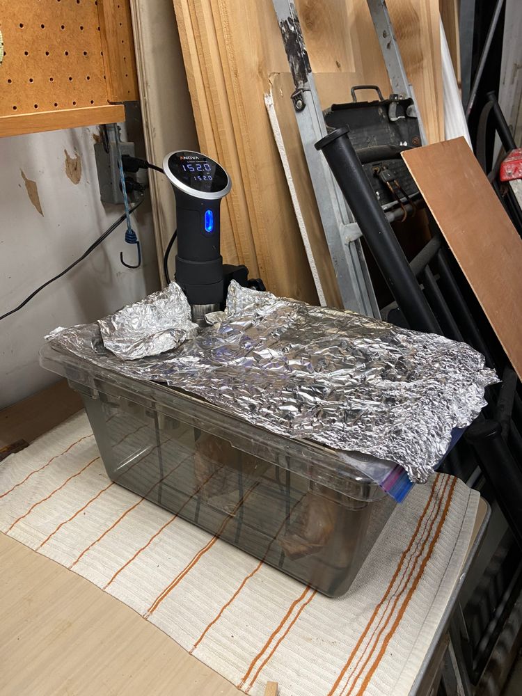 A lidded bath container covered with foil with a circulator reading 152.0°F